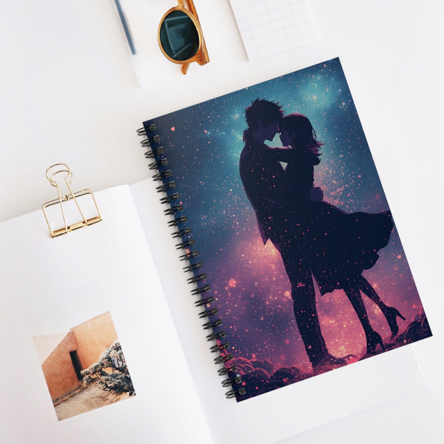 Notebook with a couple in a starry night design on a white surface with sunglasses and a photo clip.