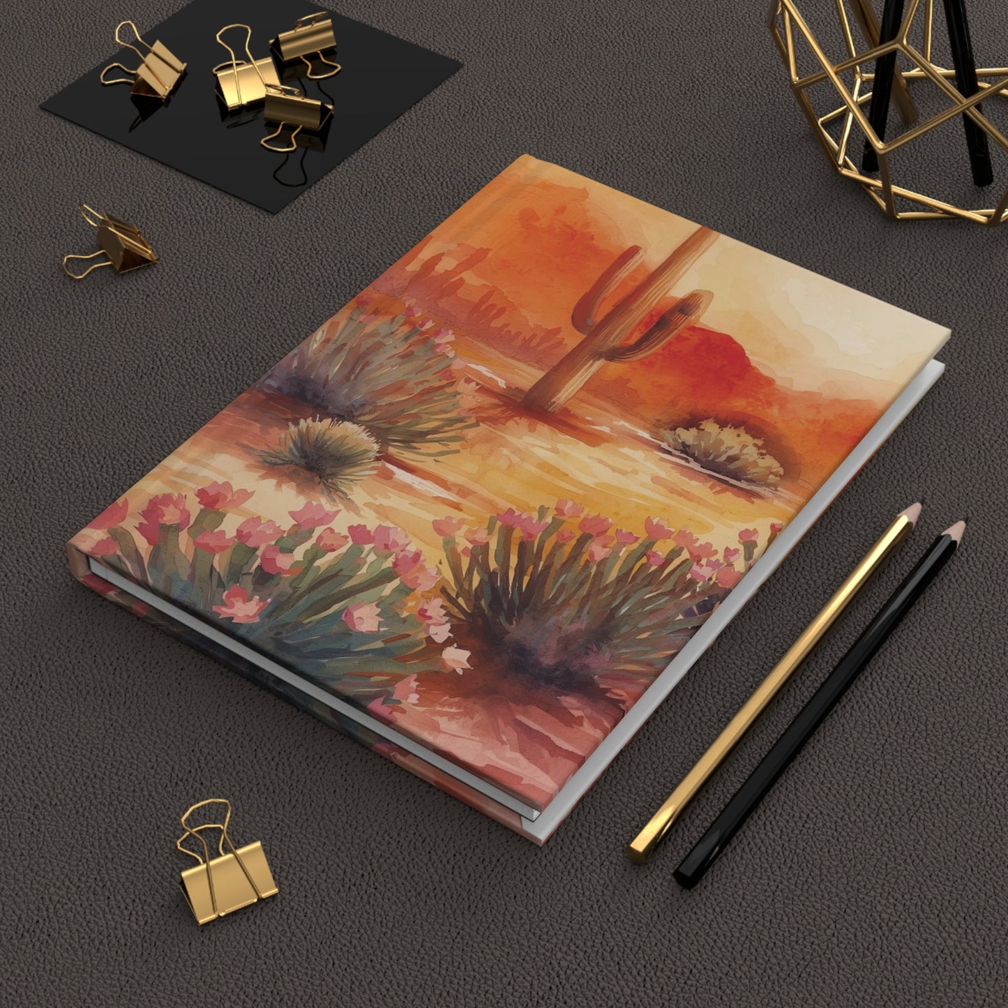 Notebook with desert landscape illustration on a dark surface with office supplies.