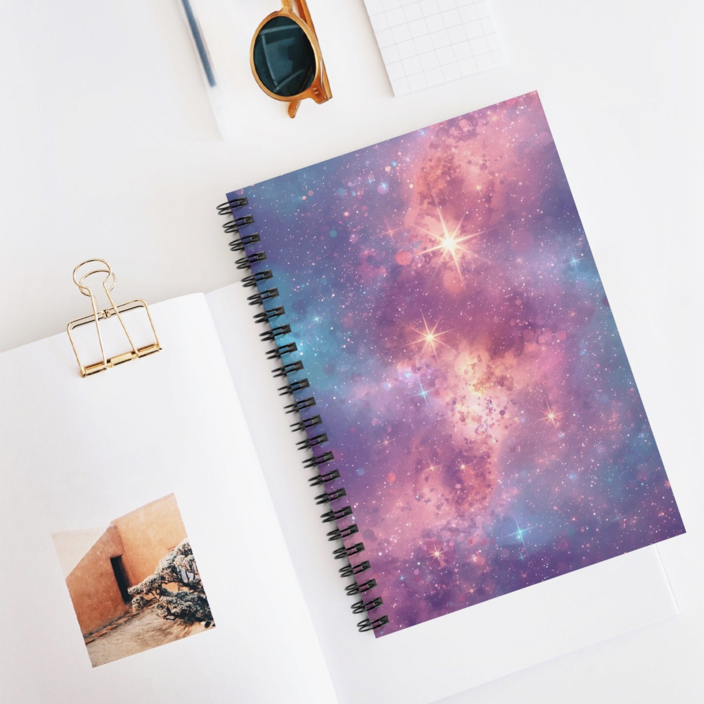 Notebook with galaxy design cover on a white surface with a photo and clip.