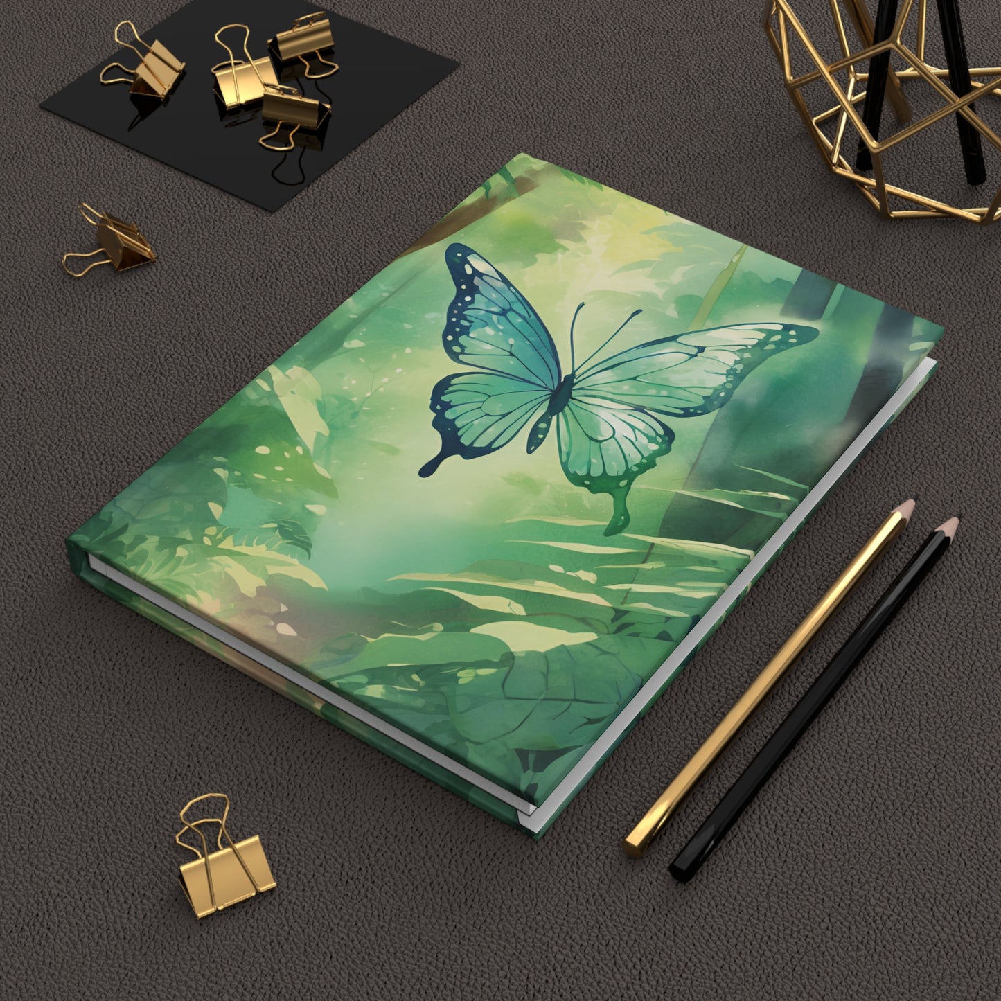Notebook with a butterfly design on a dark surface with stationery items.