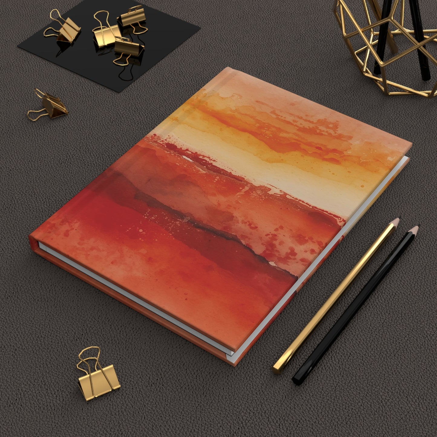 Notebook with abstract red and orange design on a dark surface with office supplies.
