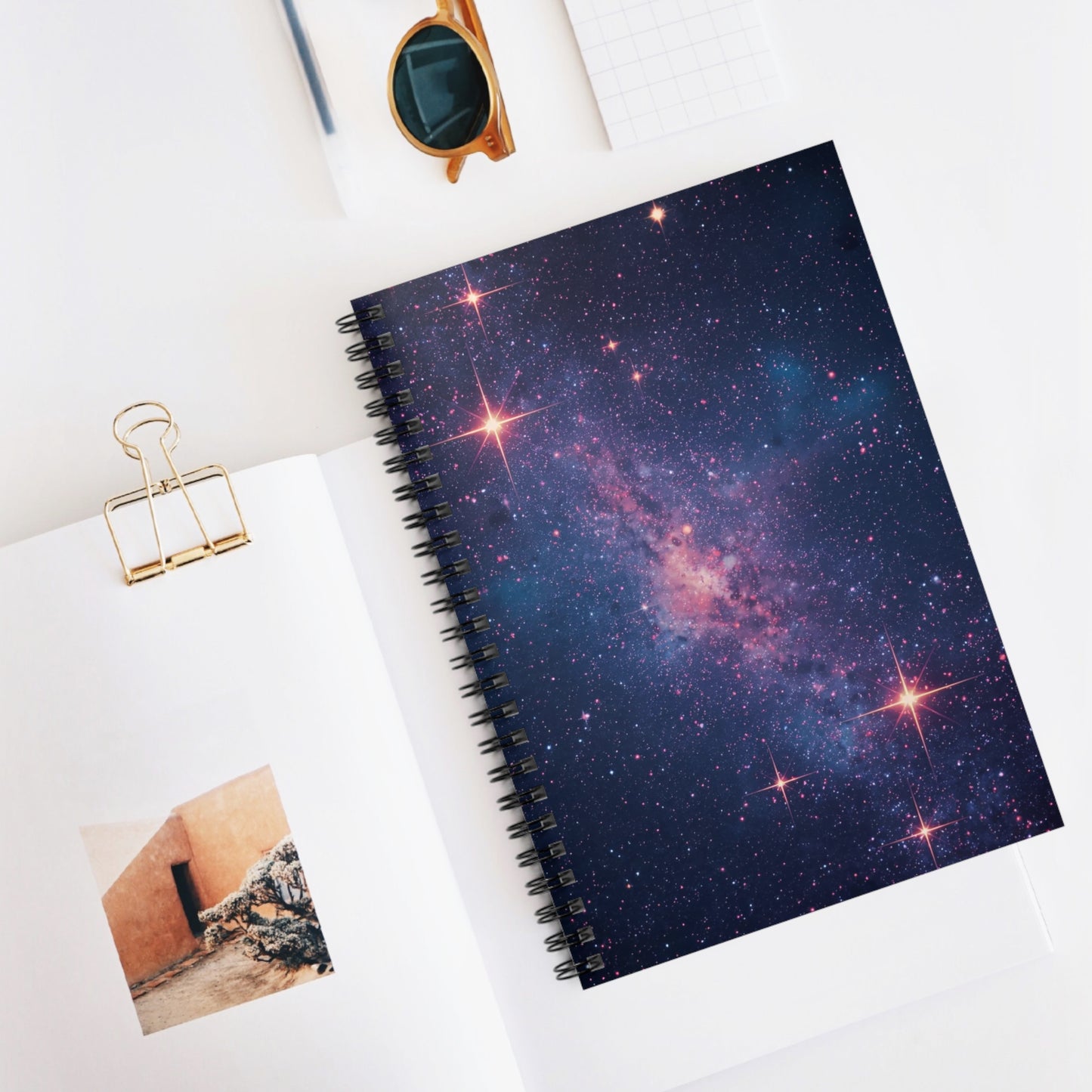 Spiral-bound notebook with galaxy design on a white surface with a photo and clip.