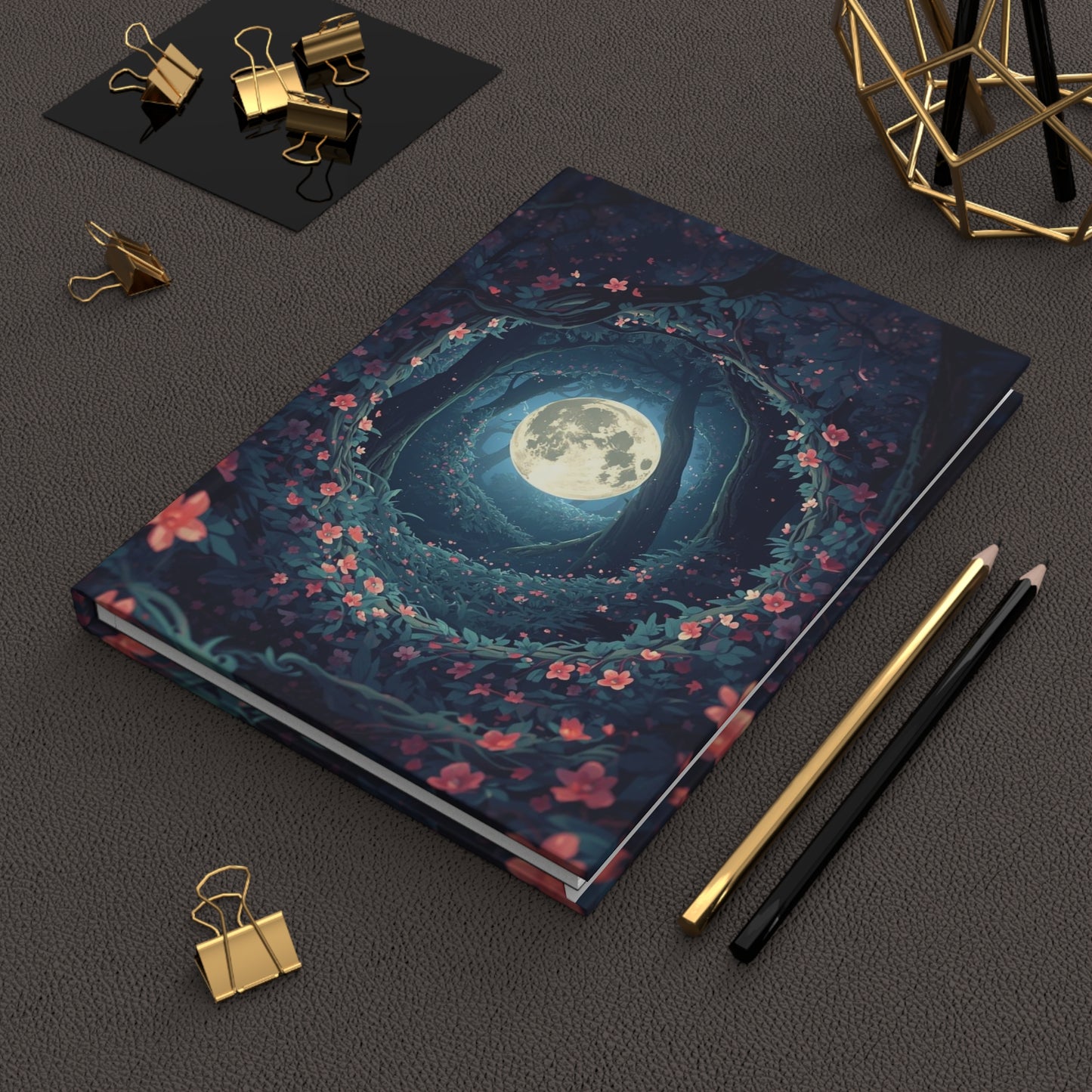 Notebook with moon and floral design on a dark surface with stationery items.