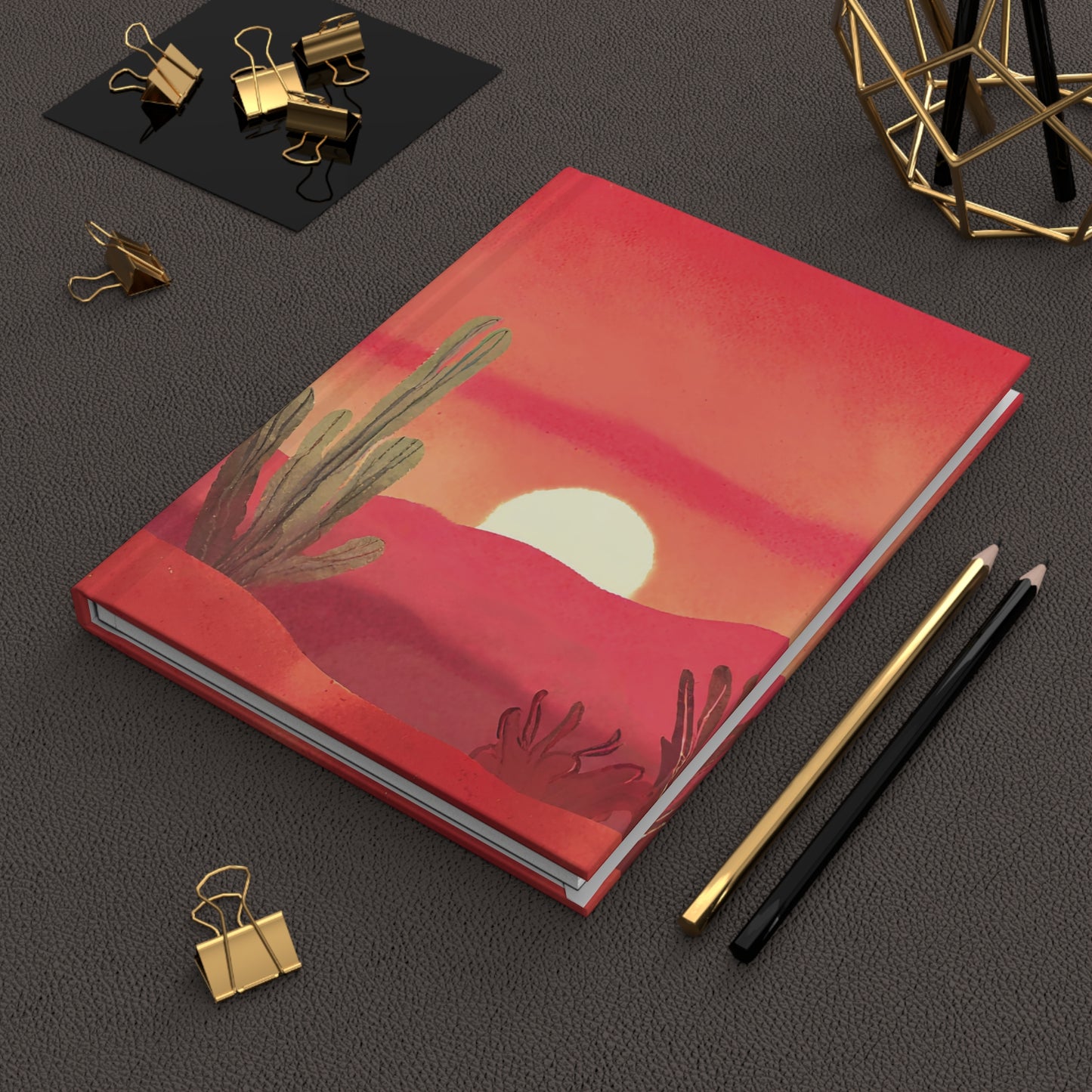 Red notebook with desert design on a dark surface with office supplies