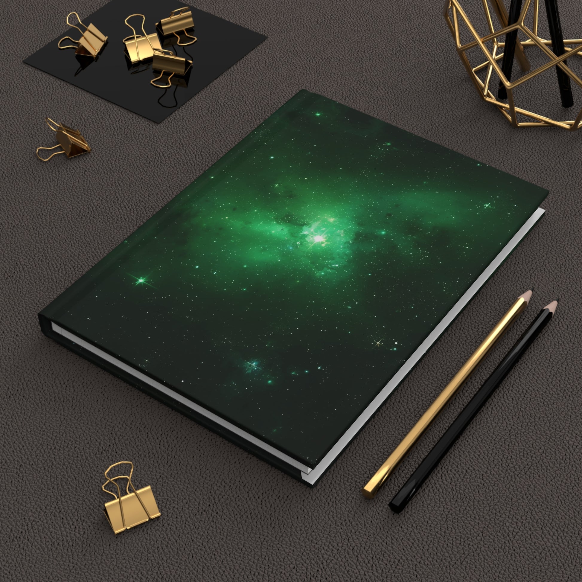 Notebook with green galaxy design on a dark surface with office supplies.