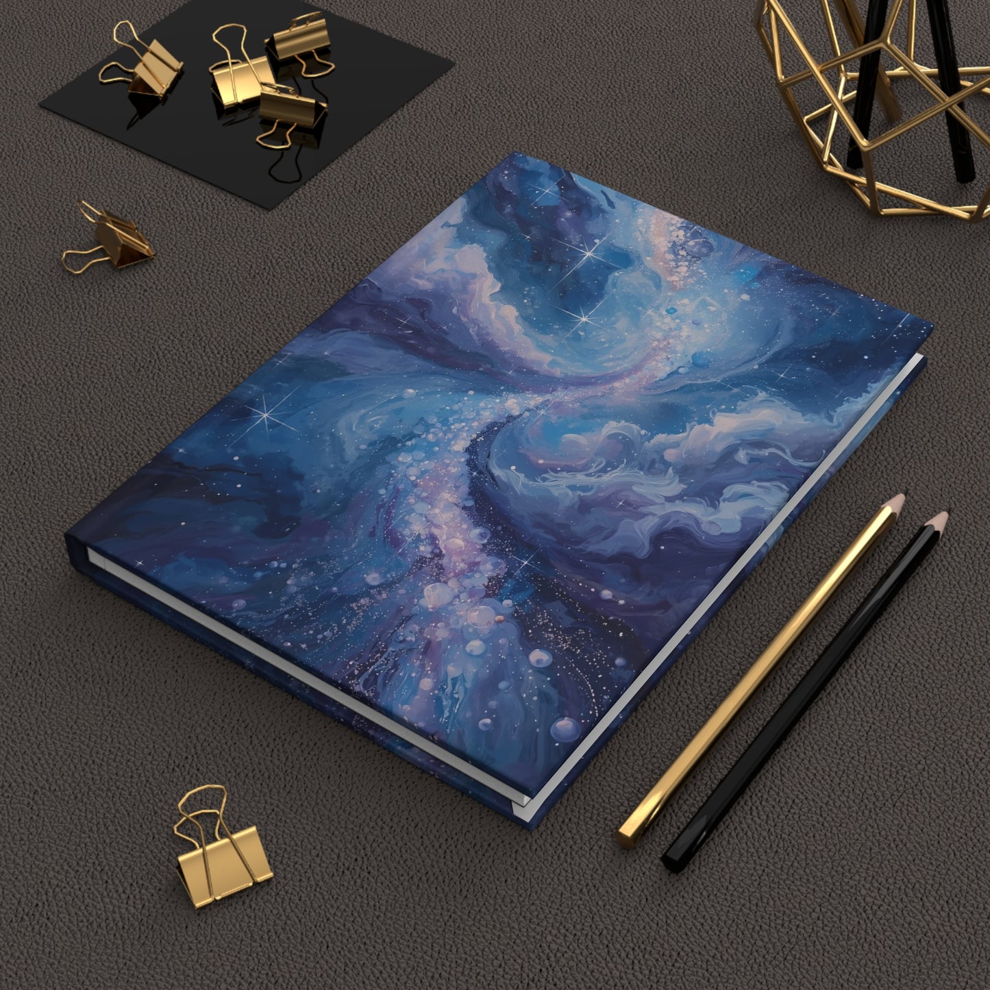 Blue notebook with artistic design on a dark surface with stationery items.