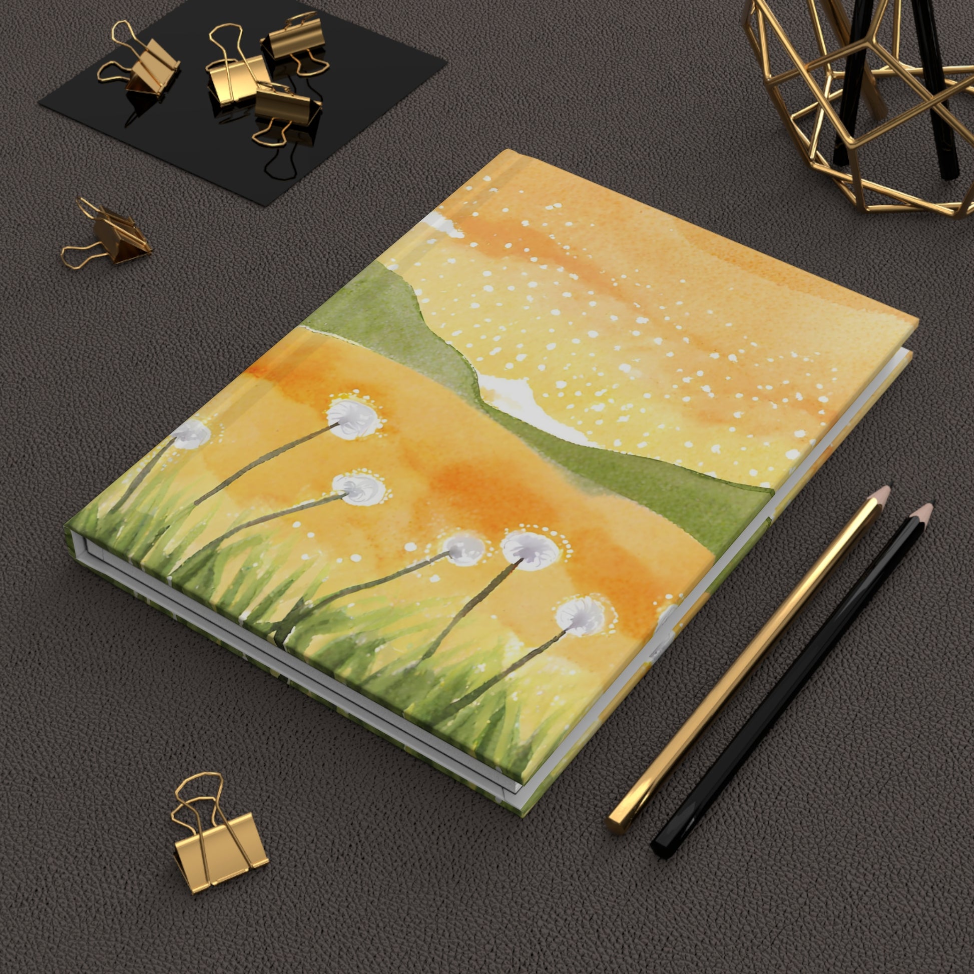 Notebook with a floral design on a dark surface with office supplies.
