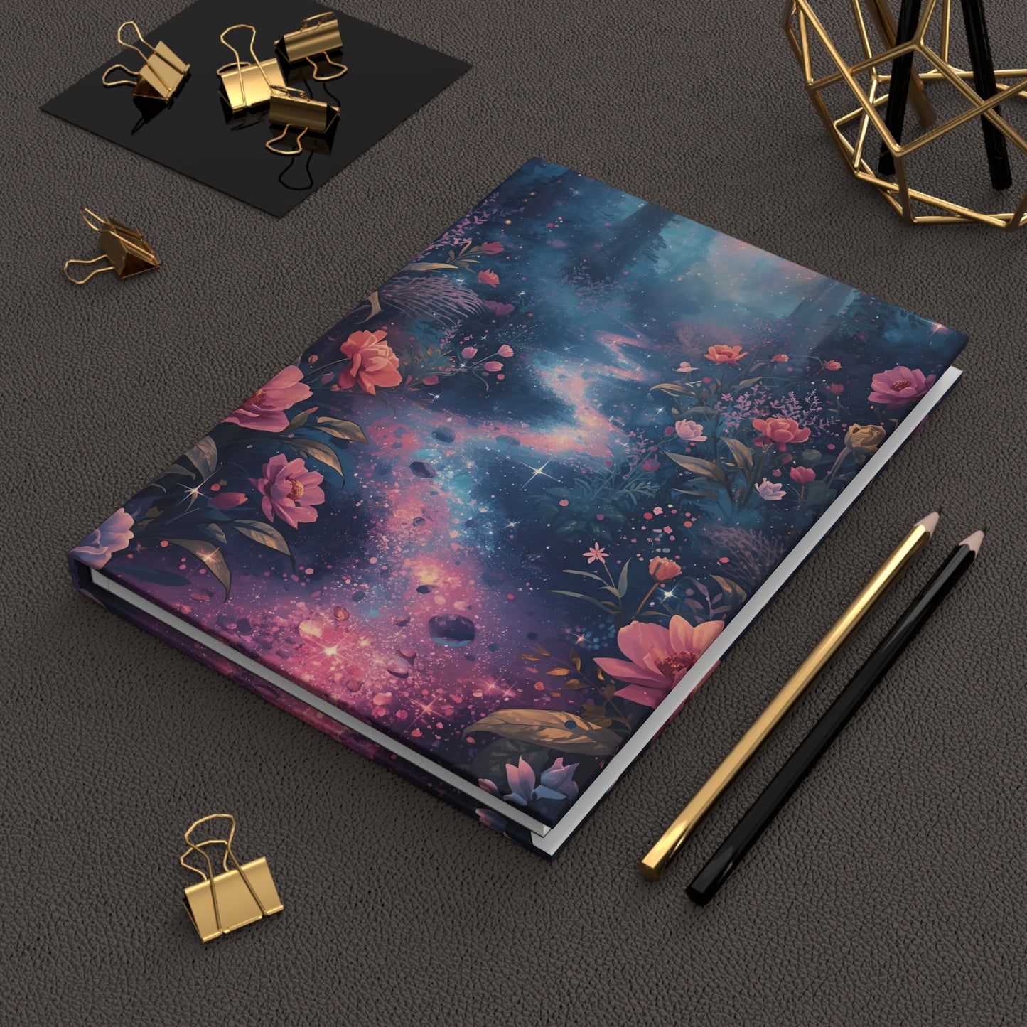 Notebook with a cosmic floral design on a dark surface with stationery items.