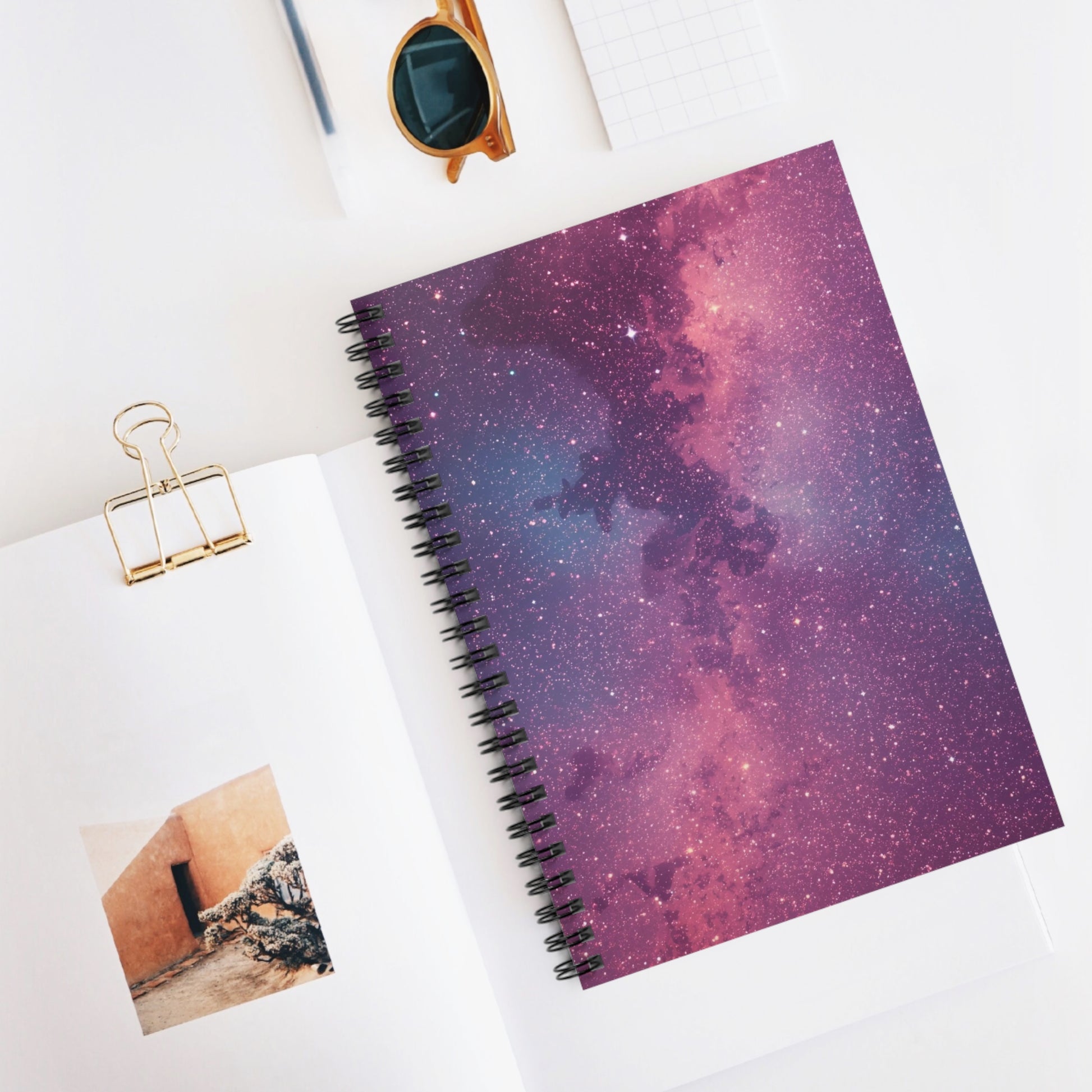 Spiral-bound notebook with galaxy design on a white surface with a photo and clip.