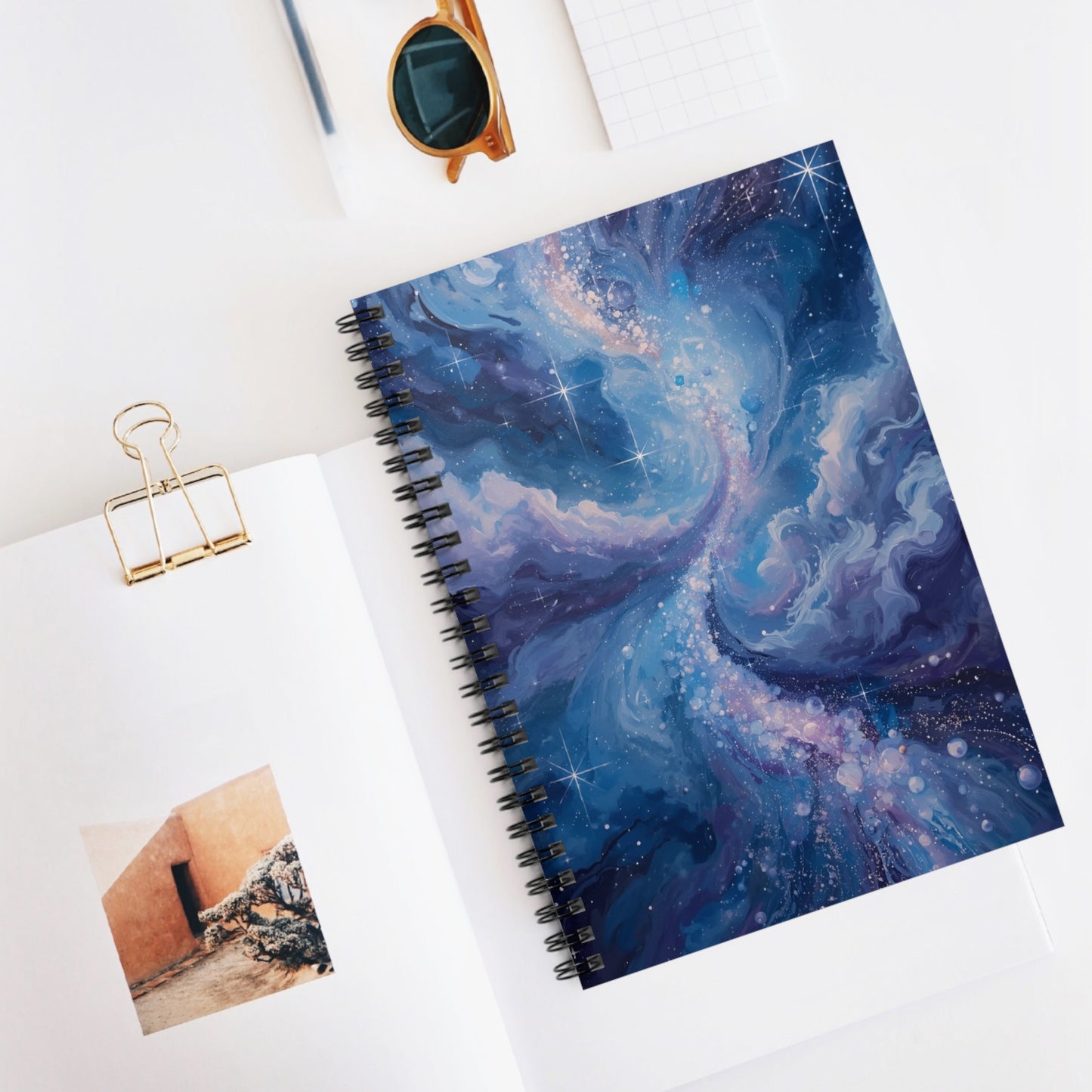 Spiral-bound notebook with a cosmic design on a white surface with a photo and clip.