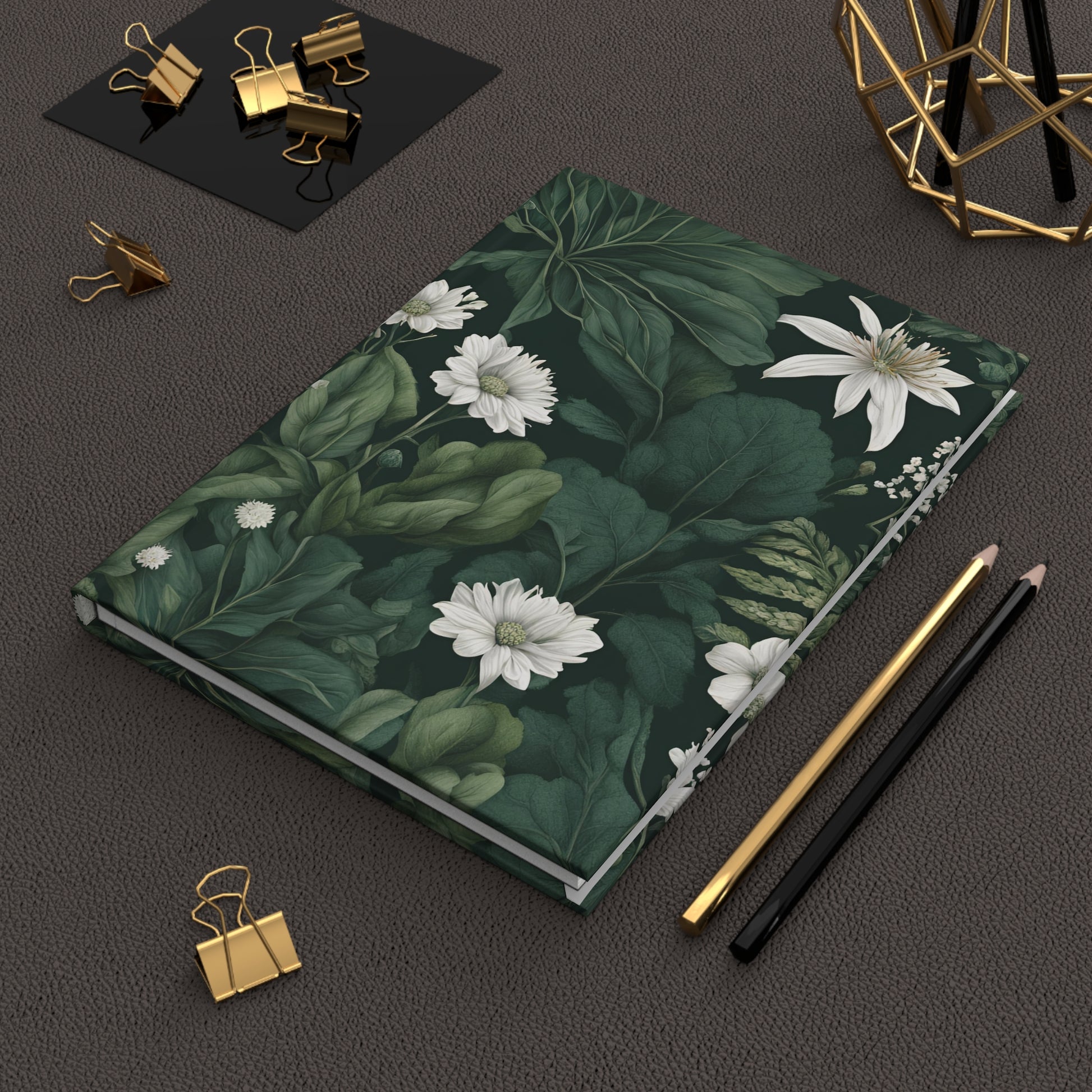 Notebook with floral design on a dark surface with stationery items.
