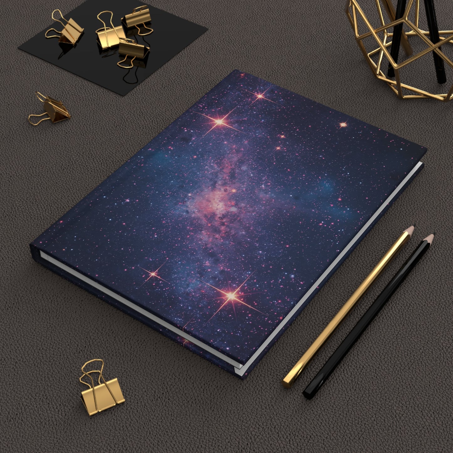 Notebook with galaxy design on a dark surface with office supplies