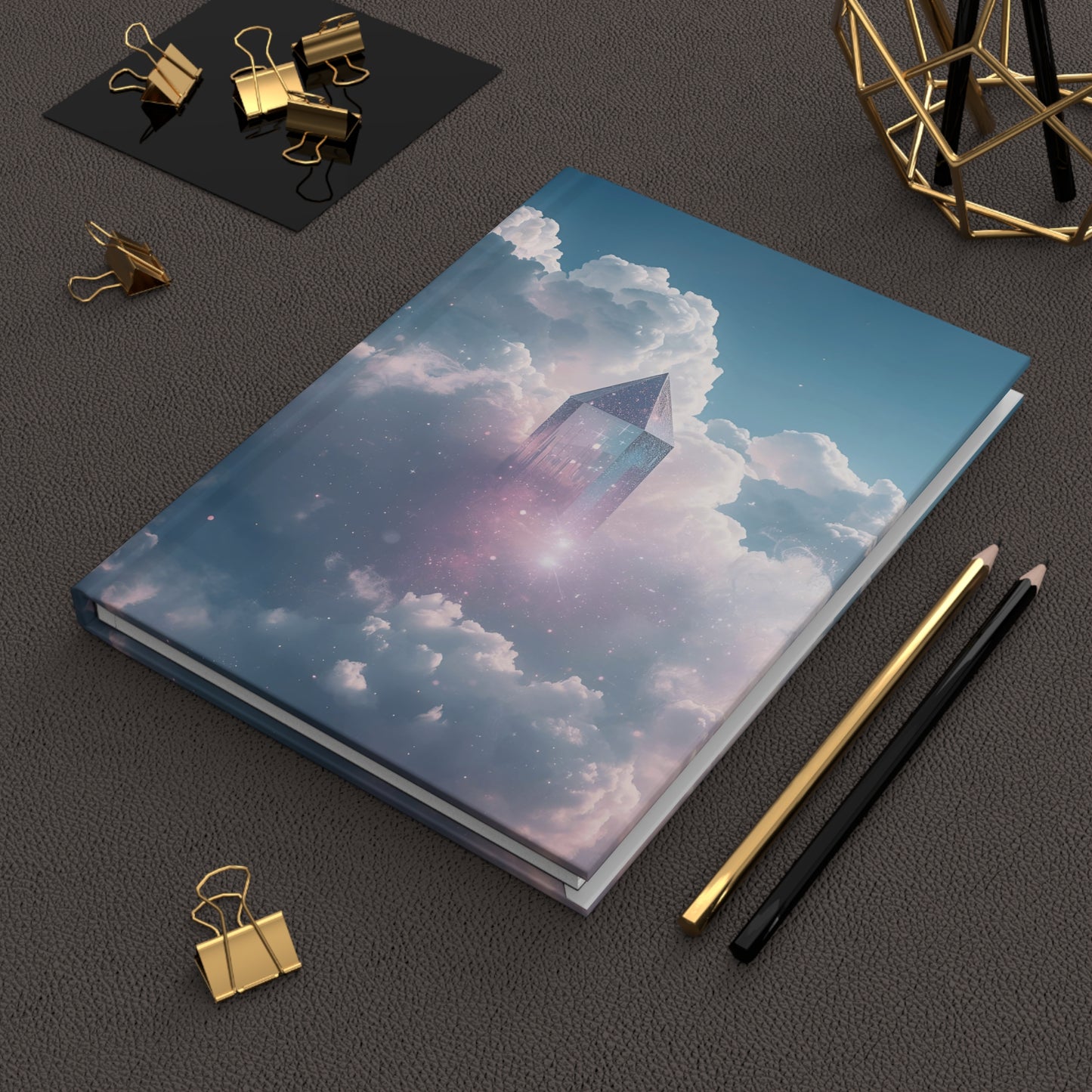 Notebook with a cloud and pyramid design on a dark surface with office supplies.
