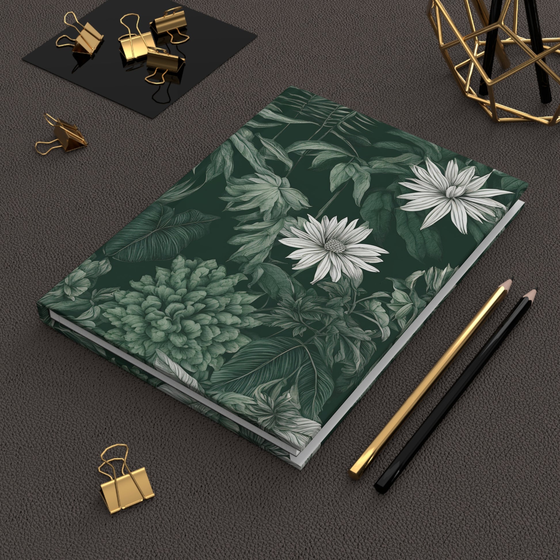 Notebook with floral design on a dark surface with stationery items.