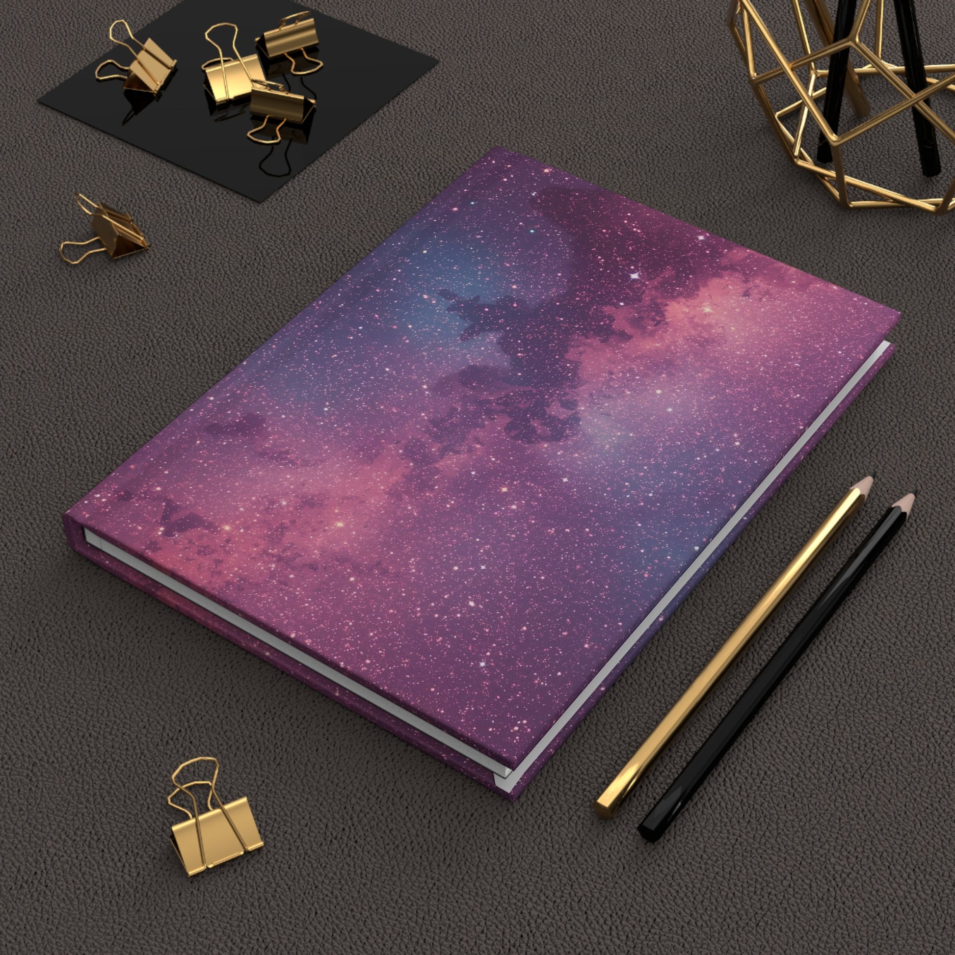 Notebook with galaxy design on a dark surface with office supplies