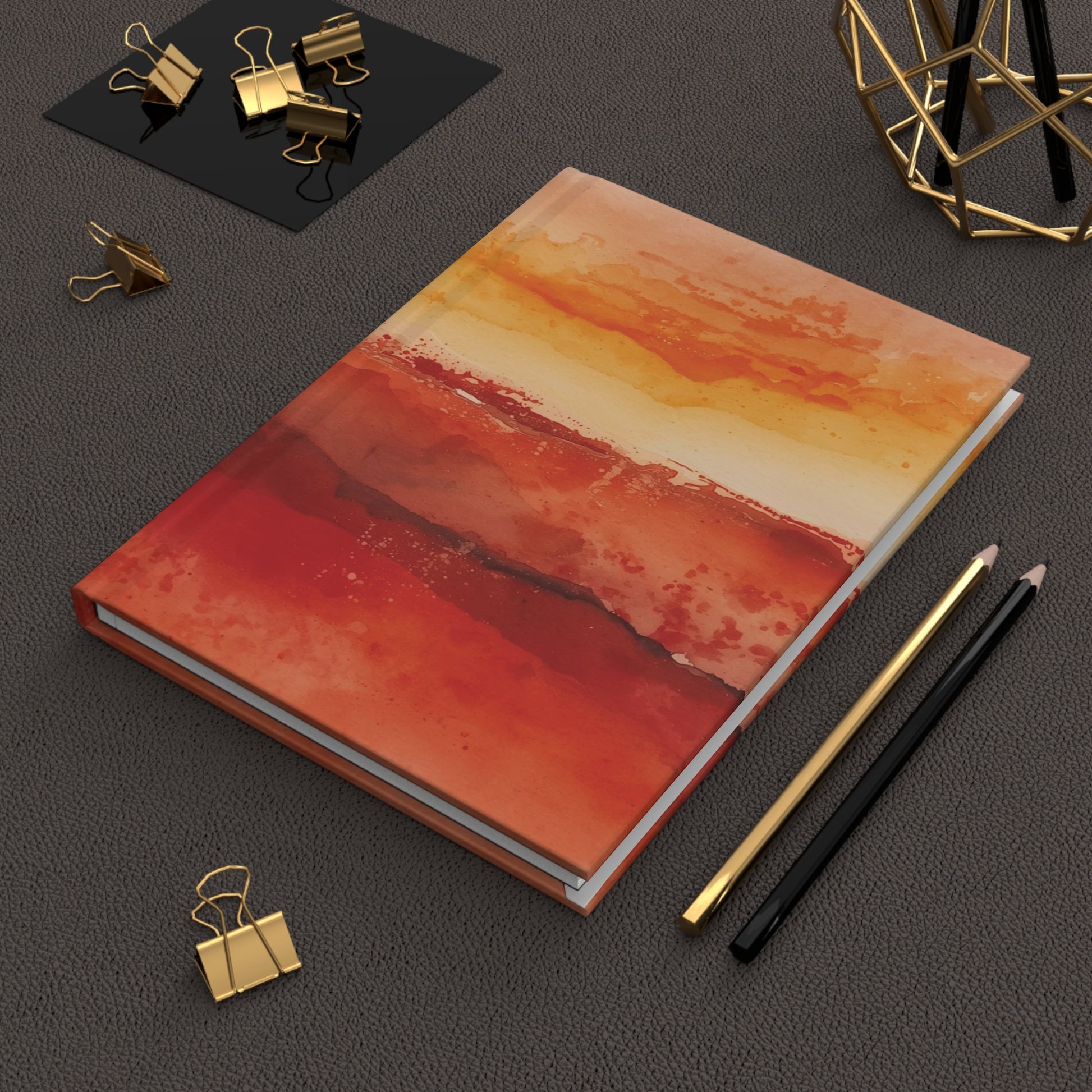 Notebook with abstract red and orange design on a dark surface with office supplies.