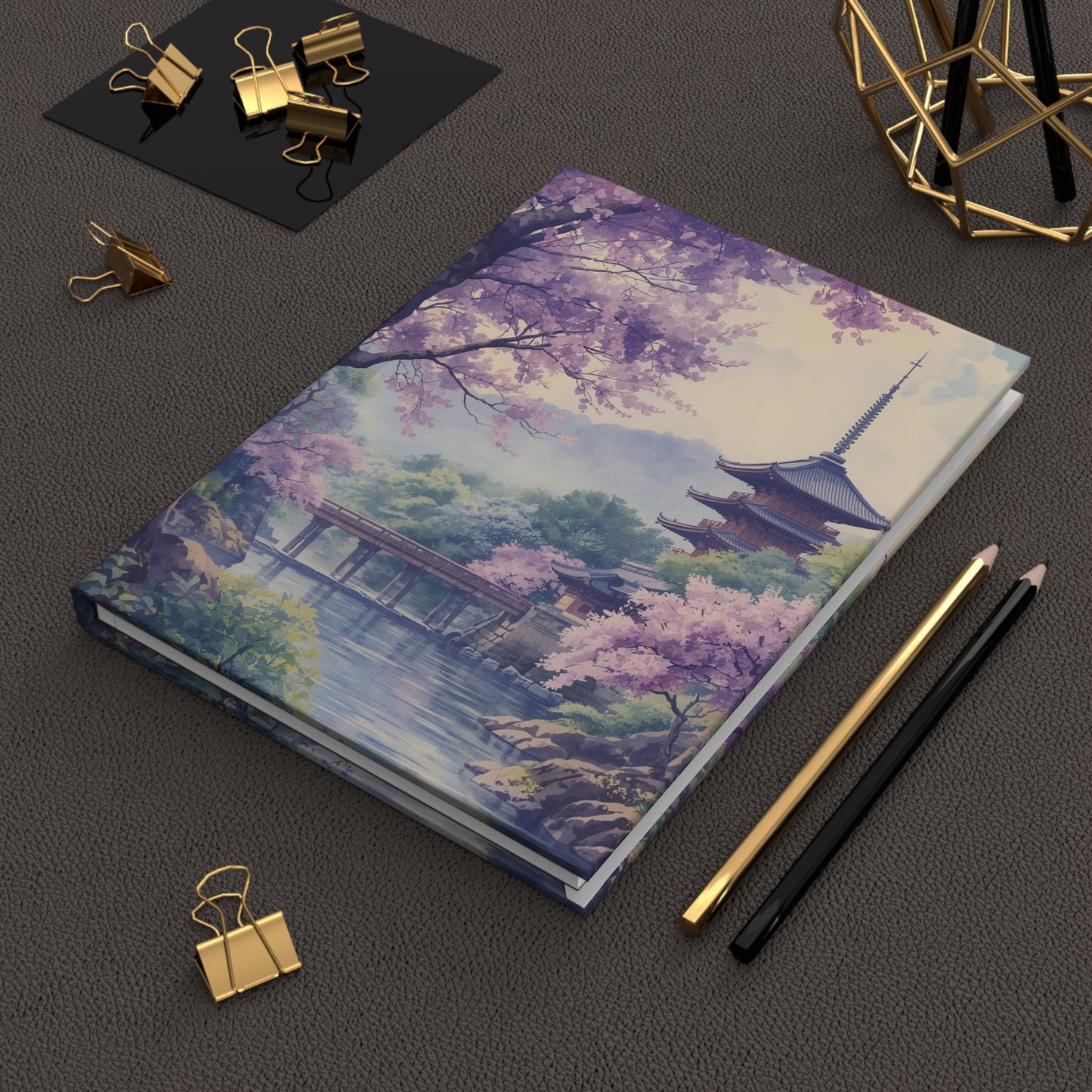 Notebook with a scenic cover featuring a pagoda and cherry blossoms on a dark surface with stationery items.