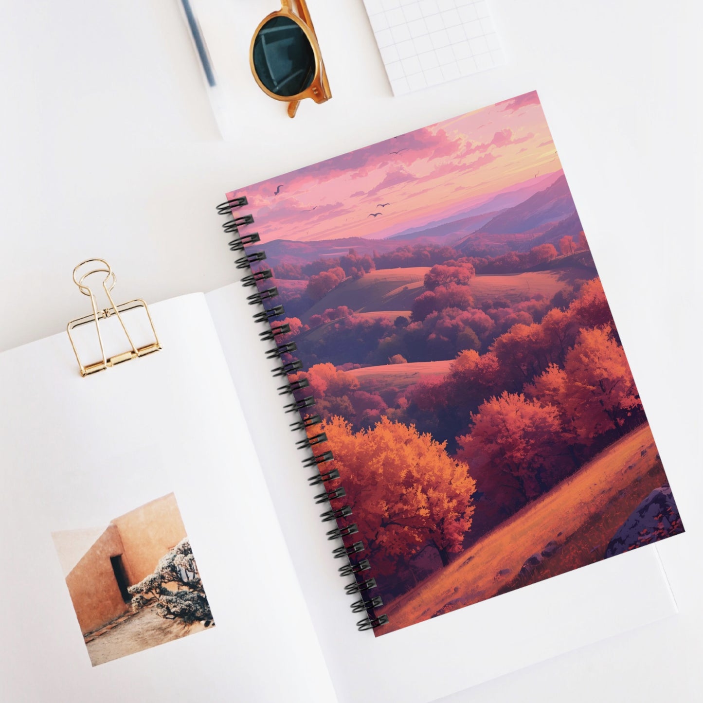 Notebook with a scenic cover on a white surface with a photo and clip.