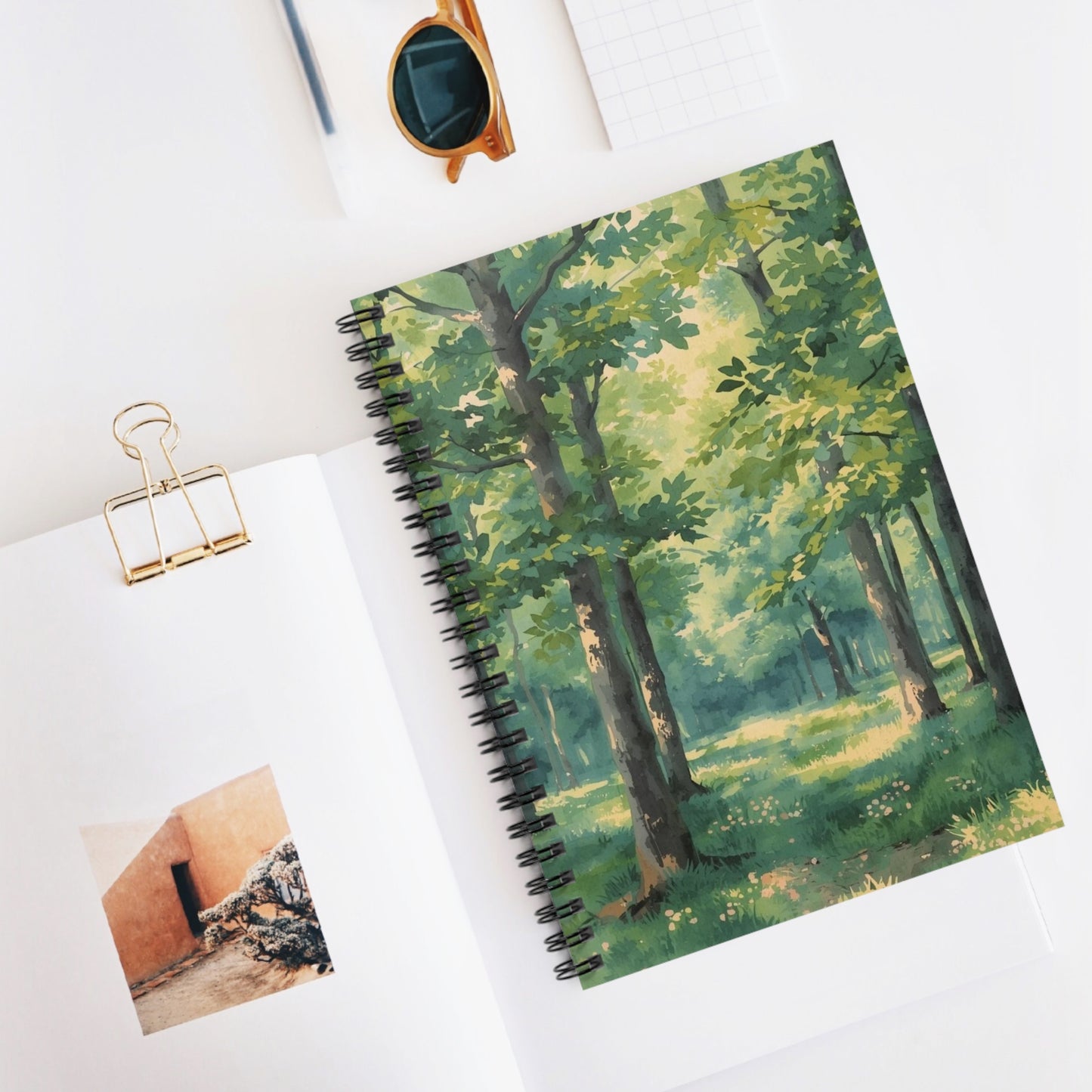 Notebook with a forest design cover on a white surface with a photo and clip.