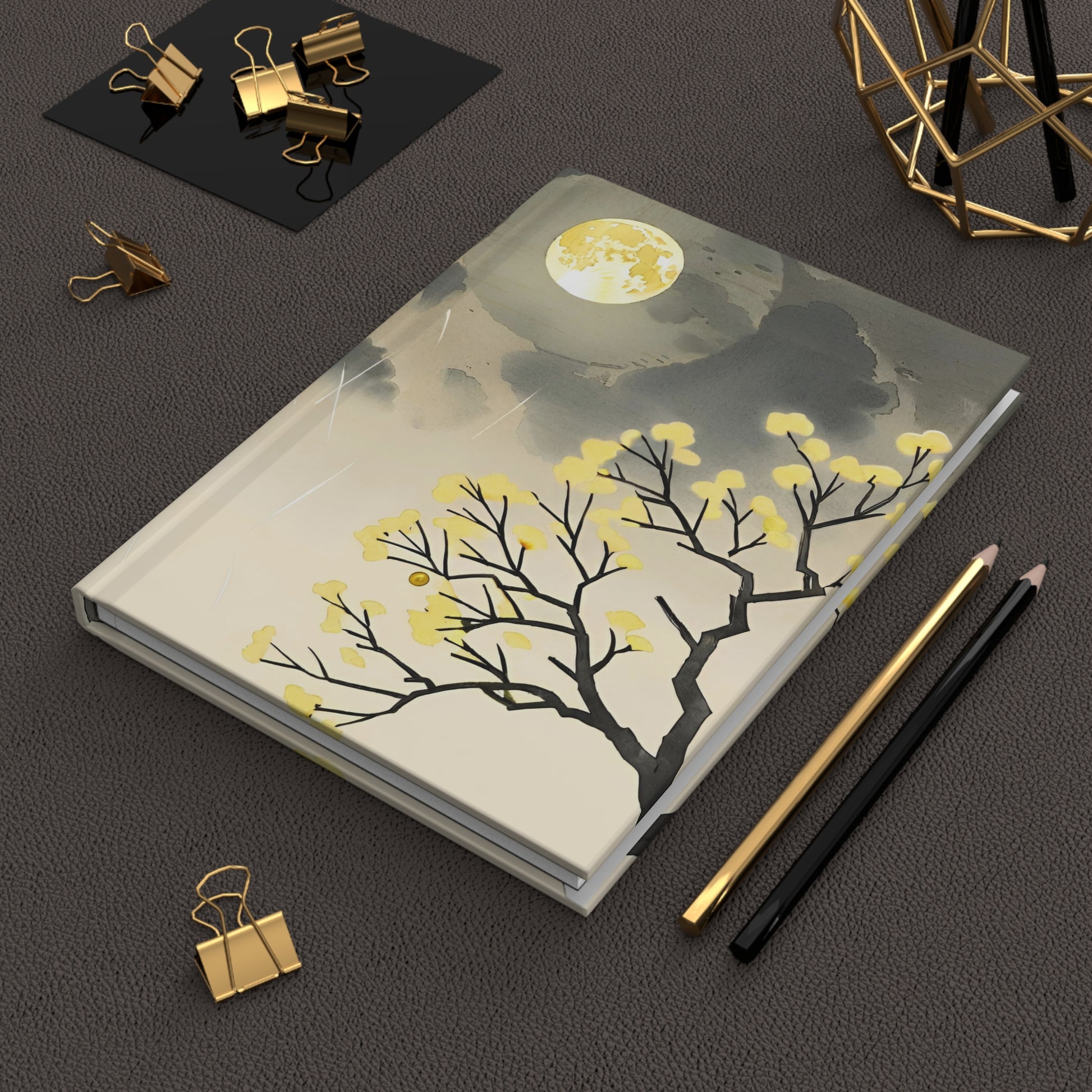 Notebook with tree design on a dark surface with stationery items